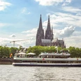 The Kölntourist passenger boat on the banks of Cologne's old town Excursion boat RheinLand in front of a large cathedral on the Rhine under an expansive summer sky