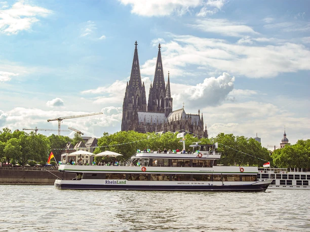 The Kölntourist passenger boat on the banks of Cologne's old town Excursion boat RheinLand in front of a large cathedral on the Rhine under an expansive summer sky