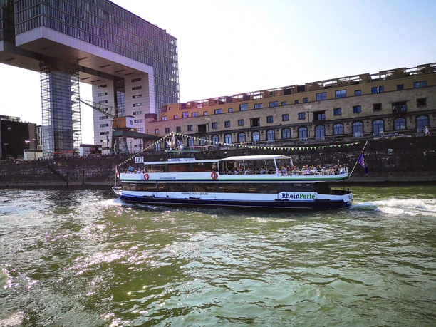 The KölnTourist passenger boat at the Rheinauhafen Excursion boat RheinPerle sails past Cologne's Rheinauhafen harbor in front of the striking crane buildings.