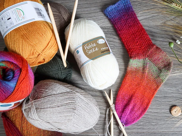 sockenwolle_knaeuel.jpg Bunte Wollknäuel mit handgestrickter Socke und Stricknadeln