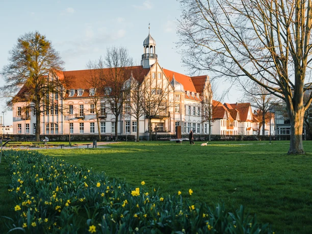 Stukenbrokpark, Post Historisches Gebäude mit rotem Dach und Turm, davor ein grüner Park mit gelben Narzissen.