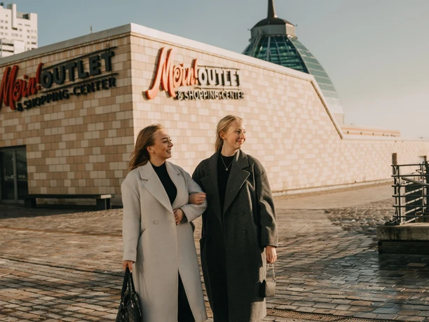 Zwei lächelnde Frauen beim Einkaufsbummel vor dem Mein Outlet & Shopping-Center in Bremerhaven