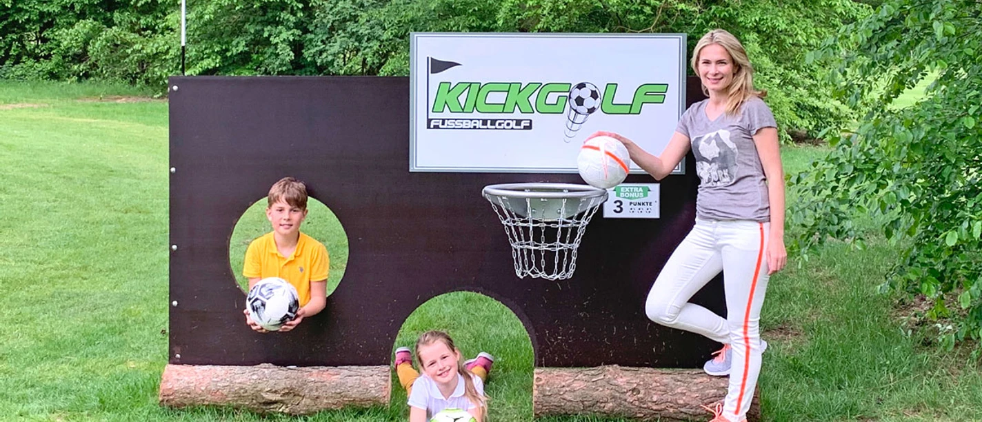 lueneburg-heide.jpg Frau und zwei Kinder mit Fußbällen an einem KickGolf-Hindernis im Grünen.
