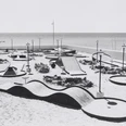 Ein schwarz-weiß-Foto zeigt eine Minigolf-Anlage mit unterschiedlichen Parcours. Im Hintergrund ist das Meer.