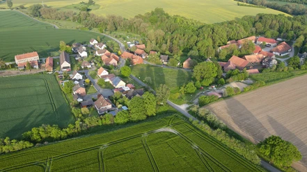Bild_Voldagsen_matthias-helmke Luftbild eines kleinen Dorfes mit roten Dächern, eingebettet in grüne Felder und Wälder.