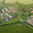 Bild_Voldagsen_matthias-helmke Luftbild eines kleinen Dorfes mit roten Dächern, eingebettet in grüne Felder und Wälder.
