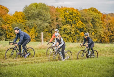 Vier Radfahrer:innen auf einer Tour im Bergischen Land im Herbst, entlang eines Feldes mit Bäumen.