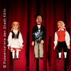 Drei traditionelle Handpuppen vor rotem Vorhang in beleuchteter Bühnenszene.