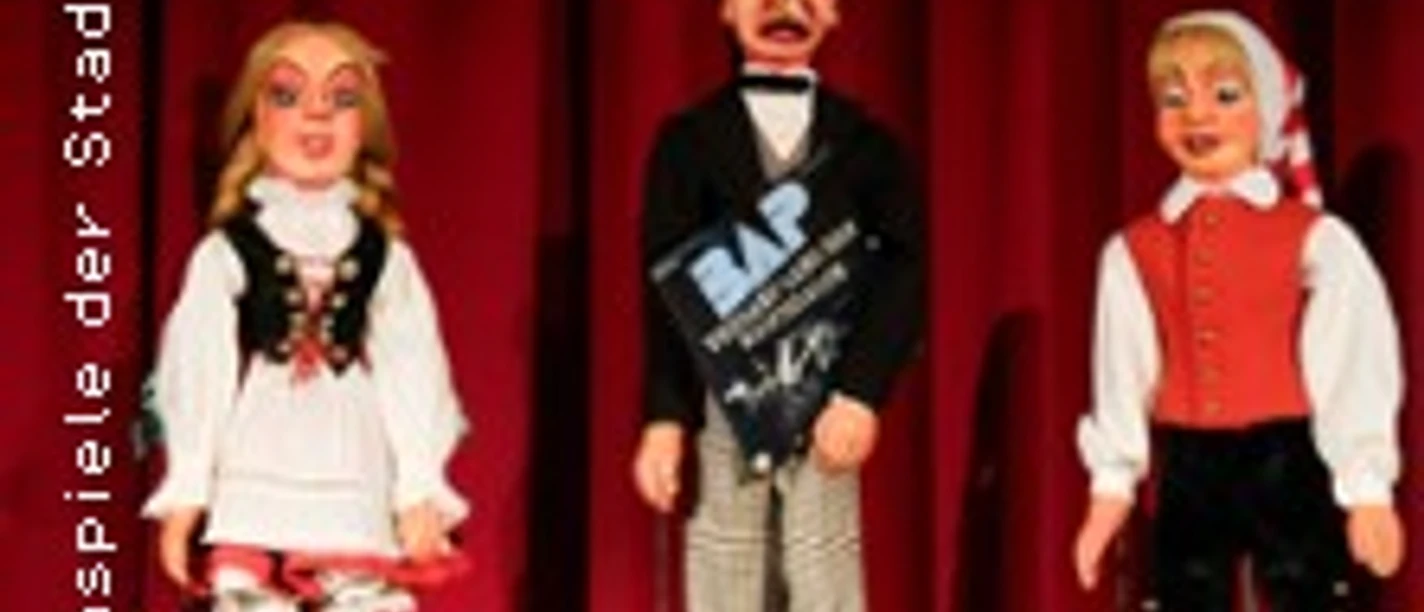 Drei traditionelle Handpuppen vor rotem Vorhang in beleuchteter Bühnenszene.