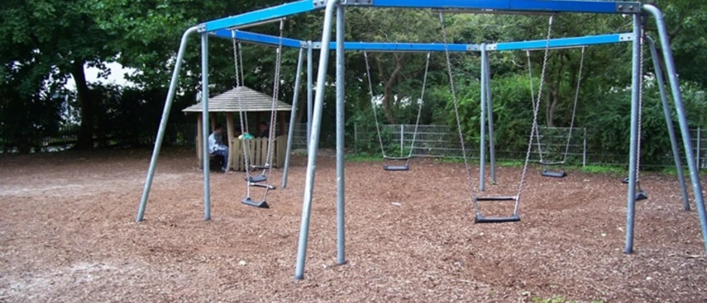 34 Danziger Platz_WEB.jpg Sechs Schaukeln auf dem Spielplatz Danziger Platz mit Schutzhütte im Hintergrund