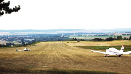 Flugplatz_Schaeferstuhl_Salzgitter_HD_16zu9.jpg Segelflugzeug und Motorflieger auf einer Graspiste vor weiter Landschaft mit Windrädern.