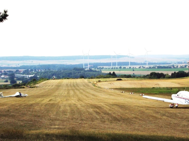 Flugplatz_Schaeferstuhl_Salzgitter_HD_16zu9.jpg Segelflugzeug und Motorflieger auf einer Graspiste vor weiter Landschaft mit Windrädern.