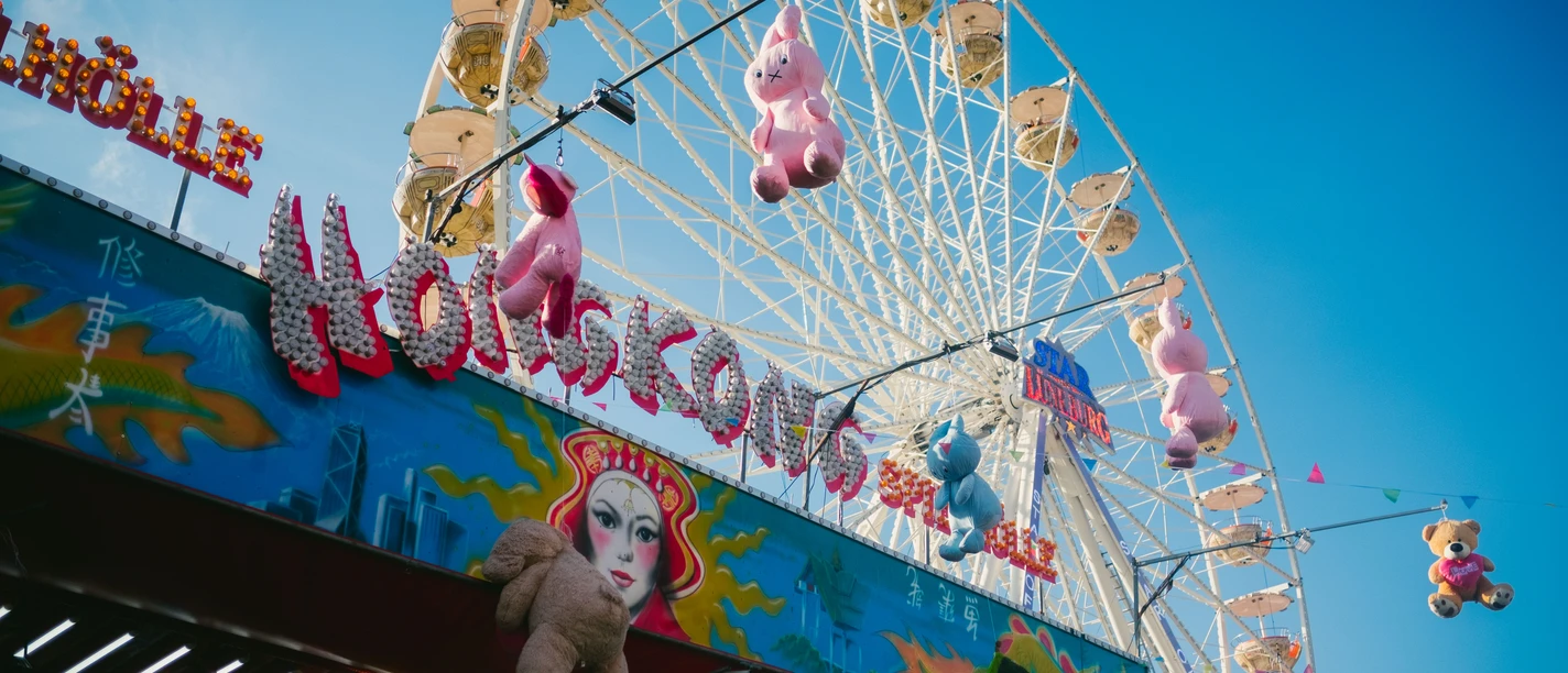 Bunte Jahrmarktsbude mit Plüschtieren vor einem großen Riesenrad unter blauem Himmel auf dem Lüneburger Frühjahrsmarkt.