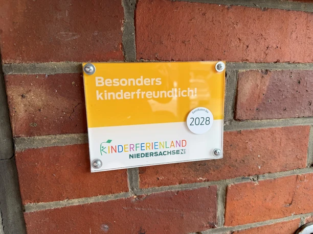 Campingplatz Stolzenau Gelbes Schild Besonders kinderfreundlich! vom Kinderferienland an einer roten Ziegelwand.
