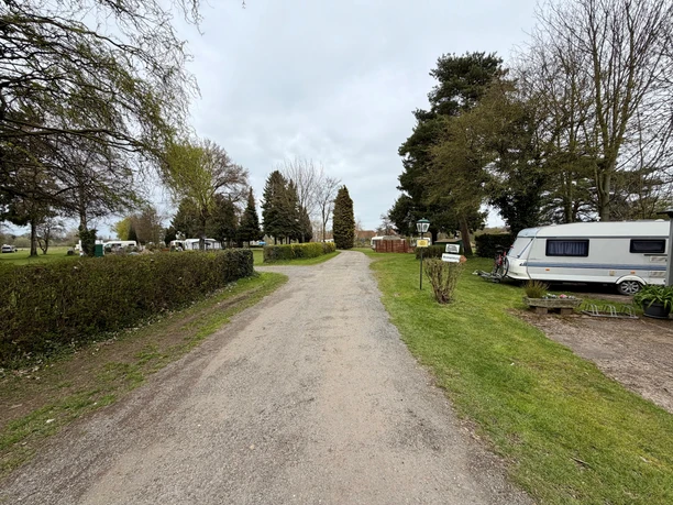 Campingplatz Stolzenau Schotterweg führt über einen grünen Campingplatz mit Bäumen und geparkten Wohnwagen.