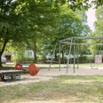 IMG_7244_WEB.jpg Wippe, Schaukel, Drehscheibe, Kletterwand und Rutsche umgeben von Bäumen auf dem Spielplatz Jakob-Kaiser-Straße
