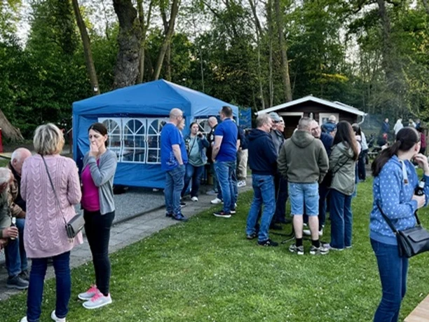 Tanz in den Mai, OBV Apen.jpeg Viele Menschen stehen auf einer Wiese vor einem blauen Zelt und feiern im Freien.