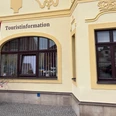 Touristinformation Neustadt Außenansicht Gelbes Gebäude mit mehreren Fenstern, Schild "Touristinformation" über dem Eingang. Rote Fahne steht davor.