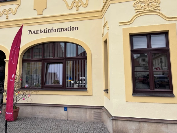 Touristinformation Neustadt Außenansicht Gelbes Gebäude mit mehreren Fenstern, Schild "Touristinformation" über dem Eingang. Rote Fahne steht davor.