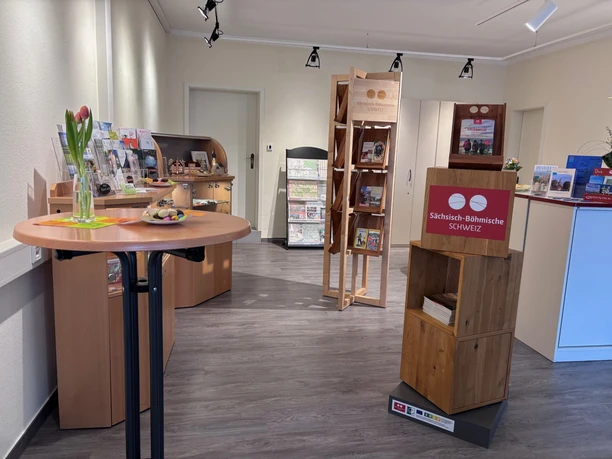 Touristinformation Neustadt Innenansicht eines Raumes mit Holzregalen, Tischen und Informationsmaterialien. Blumen in einer Vase auf einem Tisch.