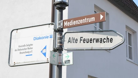 Wegweiser_AlteFeuerwache_HD_16zu9.JPG Wegweiser an einem Mast zeigt in verschiedene Richtungen, unter anderem zur Alten Feuerwache.