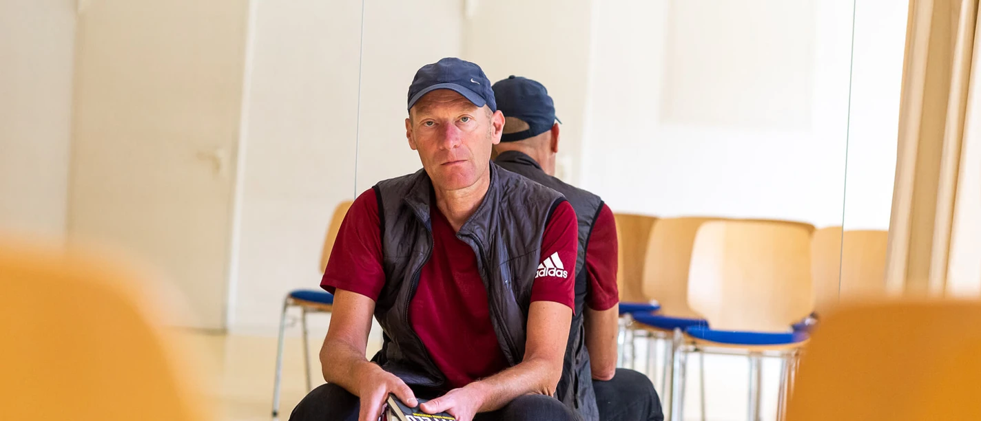 Joachim Zelter Mann mit Büchern hockt vor Spiegel in hellem Raum mit Stühlen