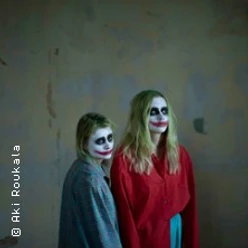 Zwei Personen mit starkem Clown-Make-up stehen vor einer schlichten Wand.