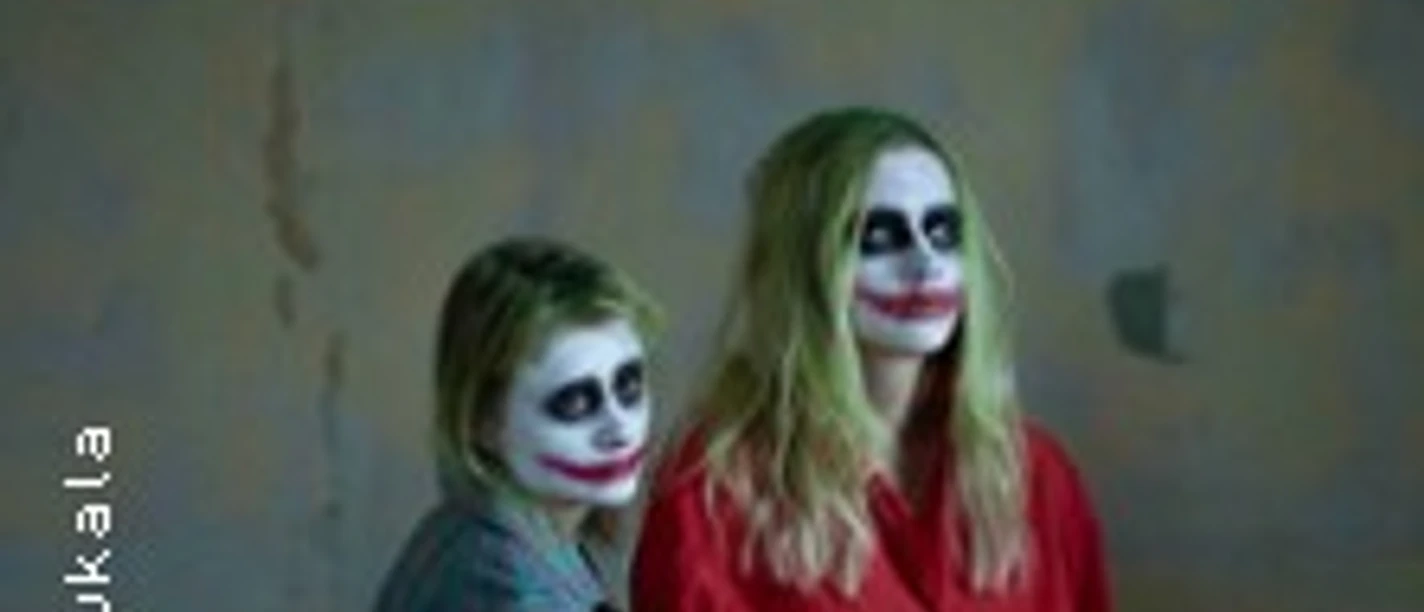 Zwei Personen mit starkem Clown-Make-up stehen vor einer schlichten Wand.