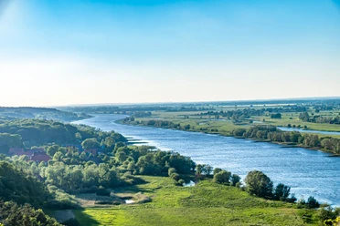 Elbekirchentag - An der Elbe.jpeg Die Elbe schlängelt sich sanft durch eine weite, grüne Landschaft unter blauem Himmel.