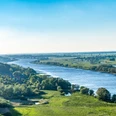 Elbekirchentag - An der Elbe.jpeg Die Elbe schlängelt sich sanft durch eine weite, grüne Landschaft unter blauem Himmel.