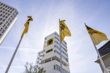 ADAC Nordrhein e.V. Gelbe ADAC-Flaggen wehen vor einem modernen Hochhaus unter klarem Himmel.