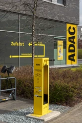 ADAC Radservice Station Gelbe ADAC-Radservicestation vor Gebäude mit Wegweiser und abgestelltem E-Scooter.
