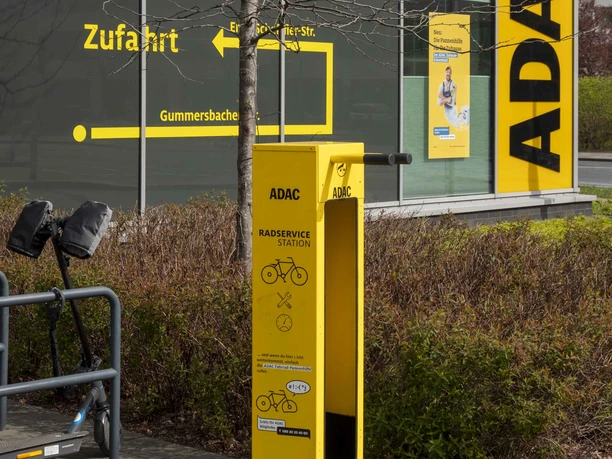 ADAC Radservice Station Gelbe ADAC-Radservicestation vor Gebäude mit Wegweiser und abgestelltem E-Scooter.