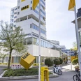 ADAC Radservice Station Gelbe ADAC‑Radservice‑Station vor dem mehrstöckigen ADAC‑Gebäude mit Fahnen und Fahrrädern.