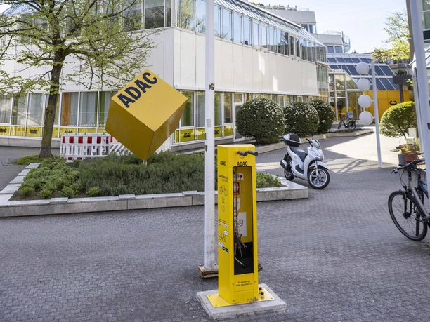 ADAC Radservice Station Gelbe ADAC‑Radservice‑Station vor dem mehrstöckigen ADAC‑Gebäude mit Fahnen und Fahrrädern.