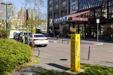 ADAC Radservice Station Gelbe ADAC-Radservicestation nahe Hoteleingang, umgeben von Autos, Fahrrädern und Grünflächen.