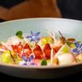 PULS - Restaurant & Bar Fein arrangierter Hummer mit Gemüse, Cremetupfen und blauen essbaren Blüten in einer Schale