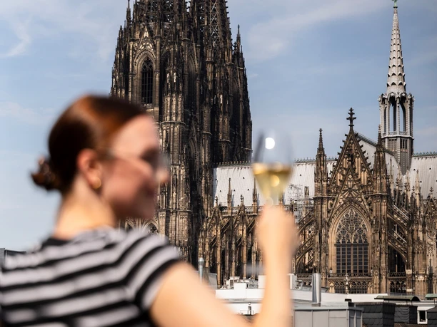 PULS - Restaurant & Bar Blurred person with glass in front of the striking towers of Cologne Cathedral on a terrace