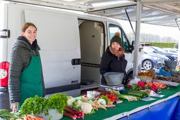 Wochenmarkt Wulsdorf S6249 (c) Helmut Gross_Erlebnis Bremerhaven.jpg Zwei Frauen hinter einem Marktstand mit frischem Gemüse wie Möhren und Blumenkohl.