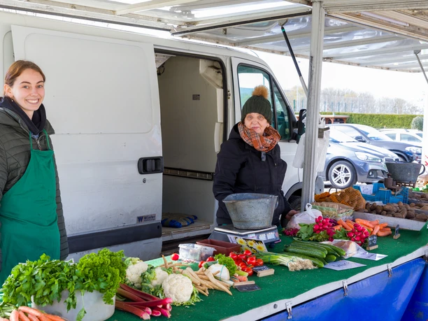Wochenmarkt Wulsdorf S6249 (c) Helmut Gross_Erlebnis Bremerhaven.jpg Zwei Frauen hinter einem Marktstand mit frischem Gemüse wie Möhren und Blumenkohl.