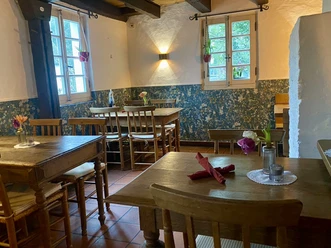 Bistrot - La Souris Rouge Rustikaler Gastraum mit Holztischen, Stühlen, Blumenarrangements und zwei hellen Fenstern.