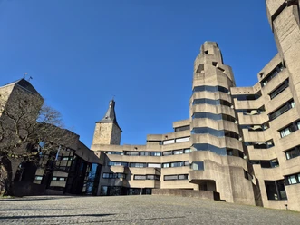 Rathaus Bensberg Rathaus Bensberg: markanter Betonbau mit geschwungenen Formen neben historischem Steinturm unter klarem Himmel.