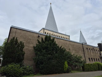 Herz-Jesu Kirche Herz-Jesu-Kirche in Bergisch Gladbach mit markanten konischen Türmen und umgebendem Grün unter bewölktem Himmel.