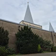 Herz-Jesu Kirche Herz-Jesu-Kirche in Bergisch Gladbach mit markanten konischen Türmen und umgebendem Grün unter bewölktem Himmel.
