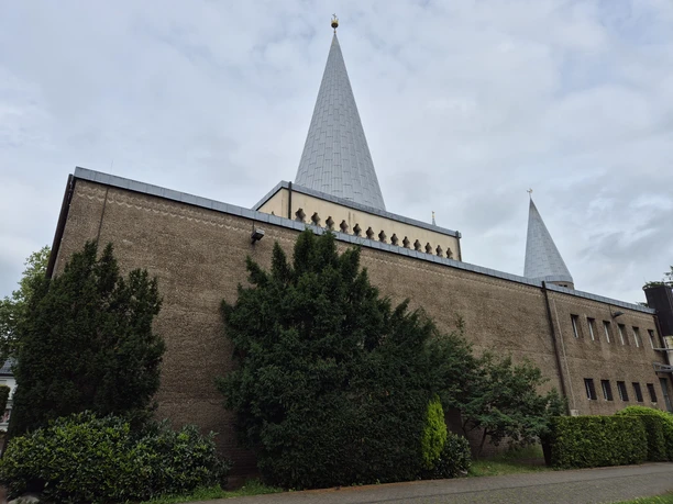 Herz-Jesu Kirche Herz-Jesu-Kirche in Bergisch Gladbach mit markanten konischen Türmen und umgebendem Grün unter bewölktem Himmel.