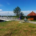 Lieblingsorte-Bokeler Brücke-Vreschen Bokel-Apen-Foto Sandra Hinrichs.jpg Radfahrer queren die Bokeler Brücke nahe einer bunten Skulptur und Holzhütte.