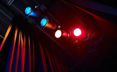 Theater K_Scheinwerfer (c) Theater K.jpg Rotes und blaues Scheinwerferlicht beleuchtet den Vorhang einer Theaterbühne.