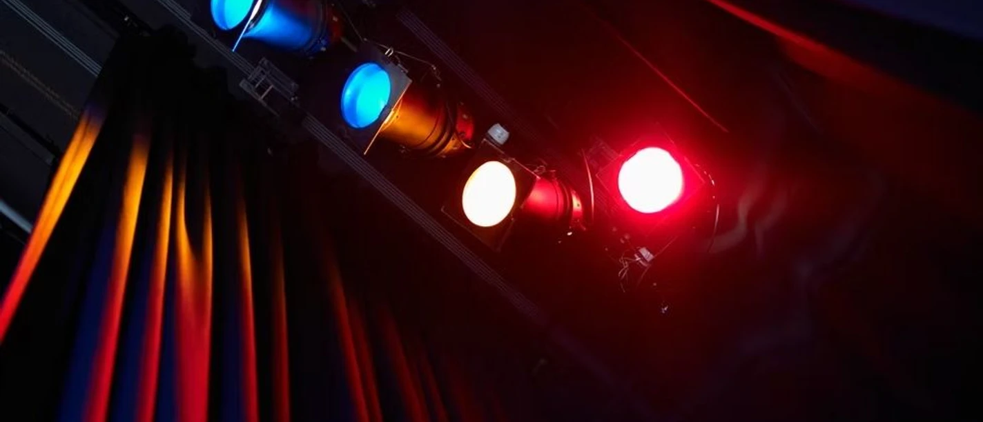 Theater K_Scheinwerfer (c) Theater K.jpg Rotes und blaues Scheinwerferlicht beleuchtet den Vorhang einer Theaterbühne.