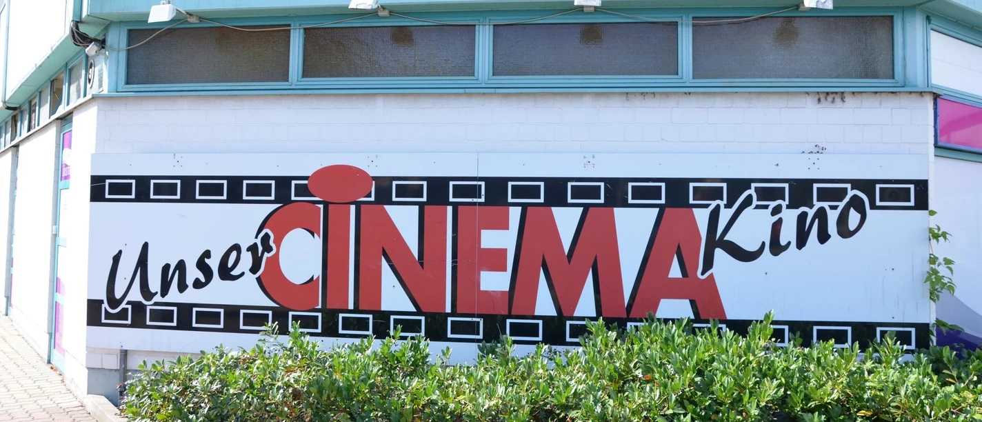 Cinema_Salzgitter_HD_16zu9.JPG Außenfassade des CINEMA Kinos in Salzgitter mit großem Logo und Schriftzug über grünem Gebüsch.