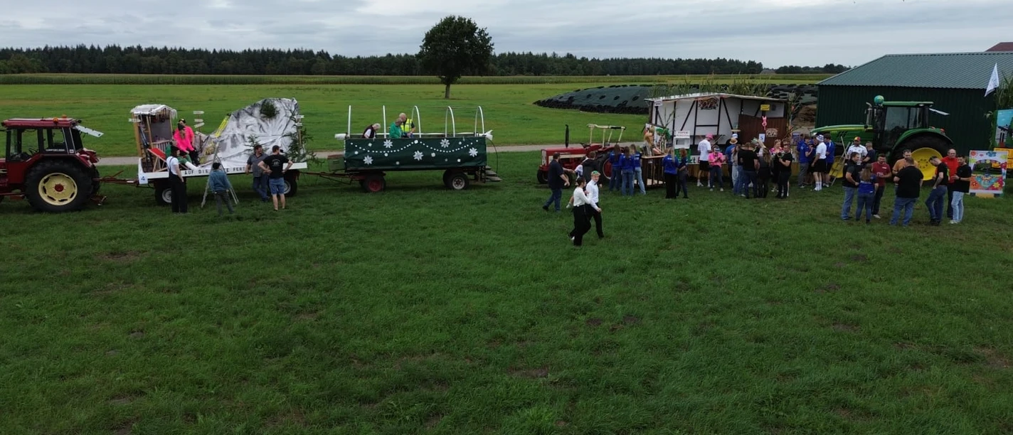 0749d52e-cabe-4d93-aea2-7d38c7ac637c.jpg Geschmückte Traktorengespanne und feiernde Menschen auf einer Wiese beim Erntefest.
